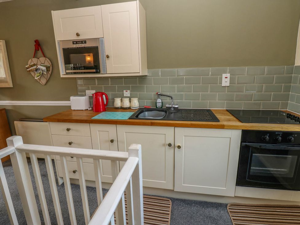 A kitchen with cabinets, stove, sink, and microwave at Kernot Cottage, Reeth