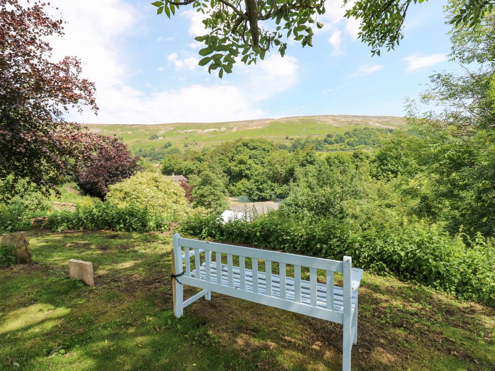 A bench in a garden with trees and mountain view at Kernot Cottage in Reeth