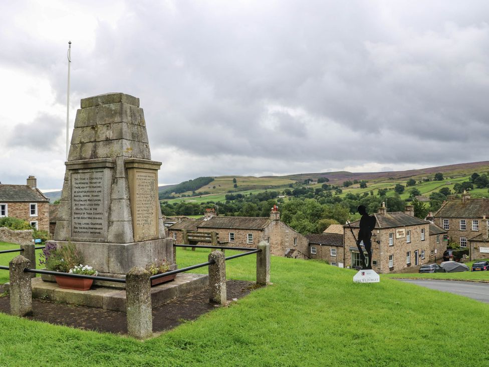 A memorial with houses and mountains in the background at Kernot Cottage in Reeth