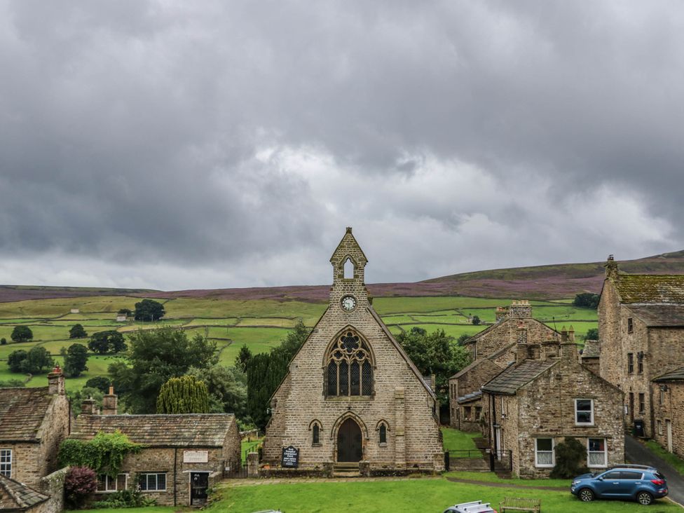A church surrounded by houses and hills at Kernot Cottage in Reeth