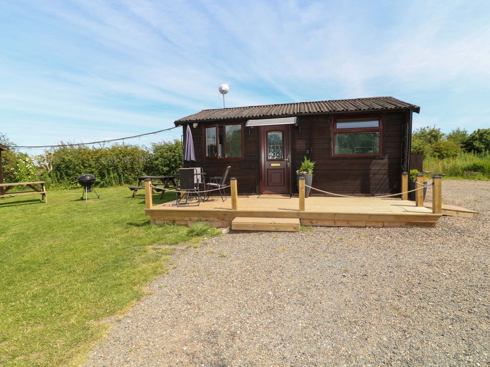 A wooden cabin with a deck and barbecue grill at Moorhen Lodge in Market Rasen