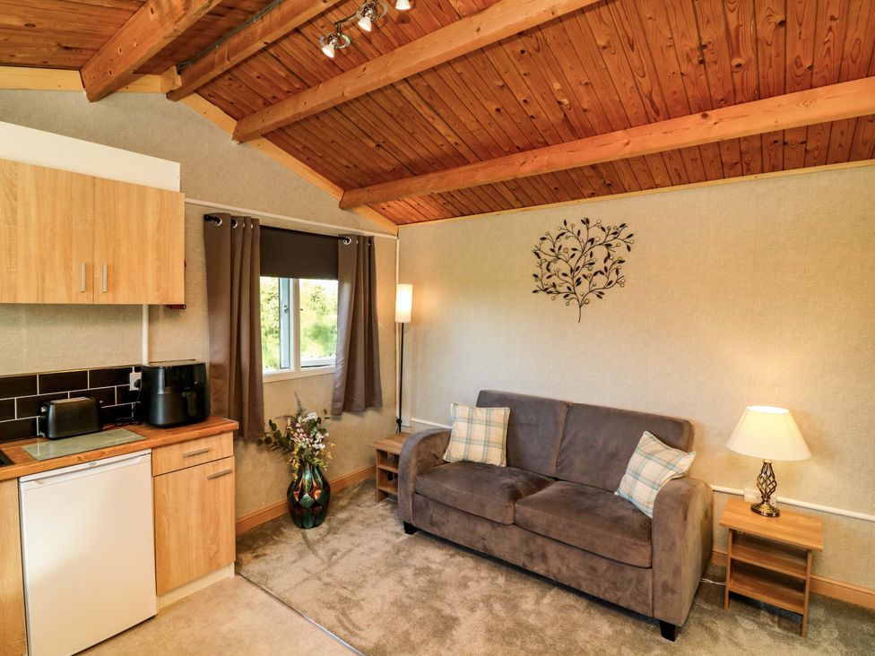 A living room with a couch and kitchen area at Moorhen Lodge in Market Rasen