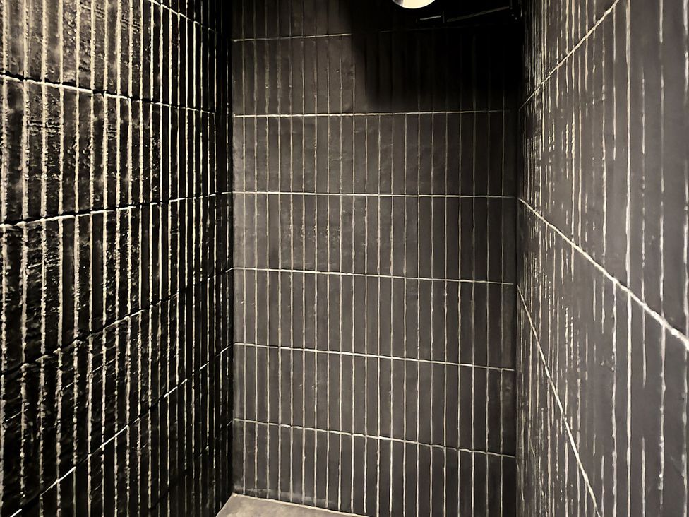 A shower with black tiled walls at Providence Cottage in Trellech