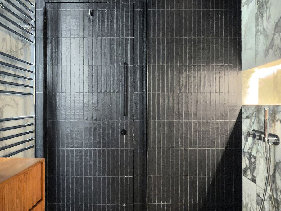 A bathroom with a black door and tiled wall at Providence Cottage in Trellech