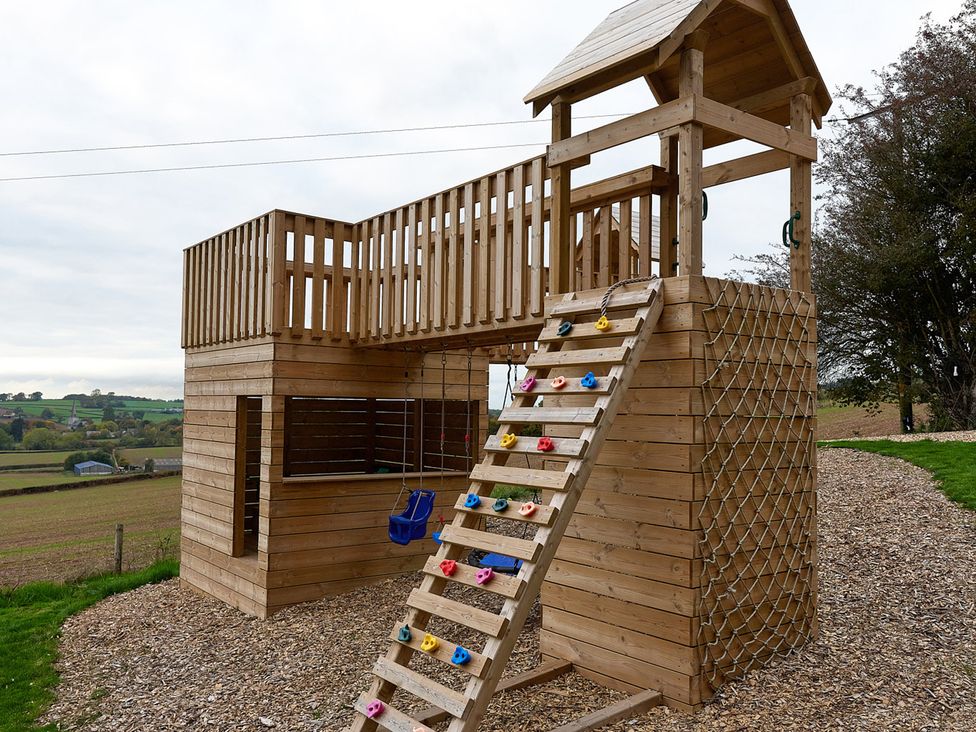 A playhouse with a climbing wall and swing in an outdoor play area at Providence Cottage Trellech