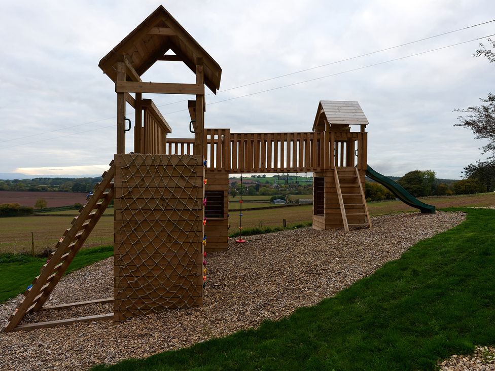 A wooden playhouse with a slide and climbing wall in a playground at Providence Cottage Trellech