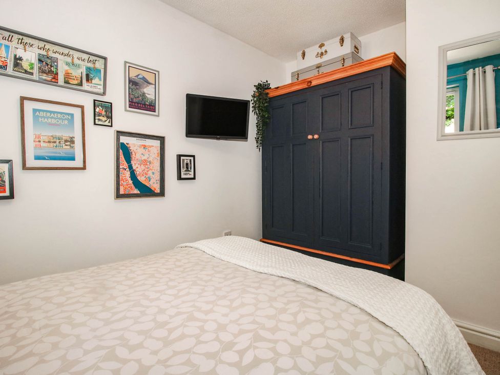 A bedroom with a bed, wardrobe, and framed pictures at Lilac Cottage in Ironbridge