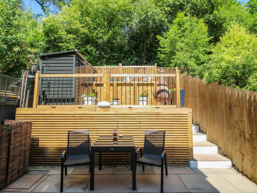 A garden with a table and chairs in front of a wooden decking area at Lilac Cottage in Ironbridge