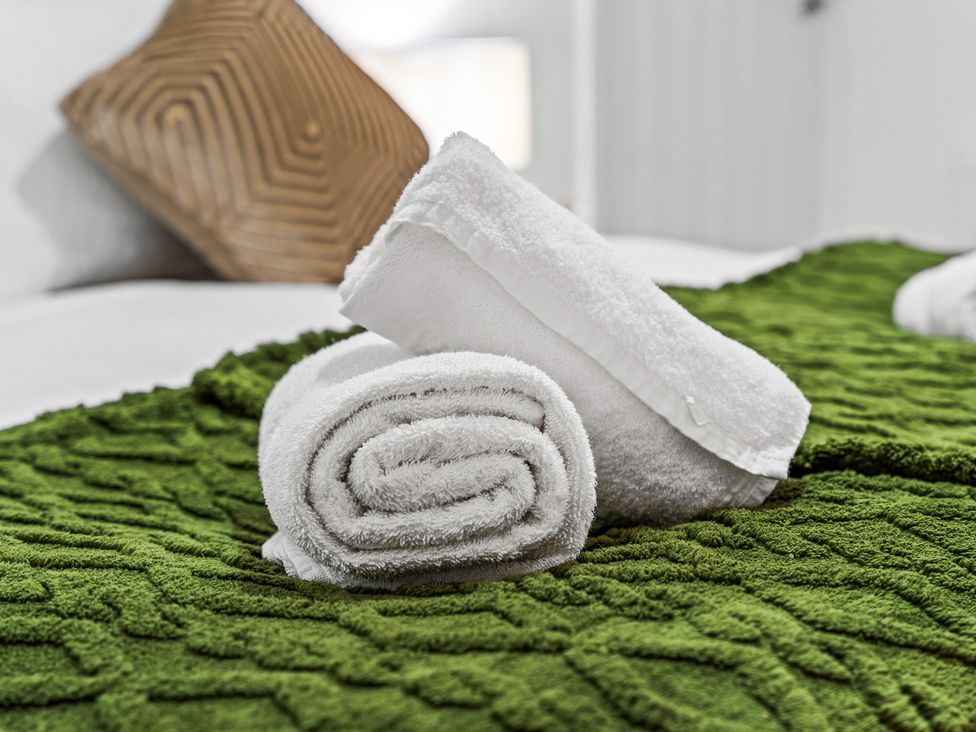 A bedroom with rolled towels on a green bedspread at Edison House Stafford