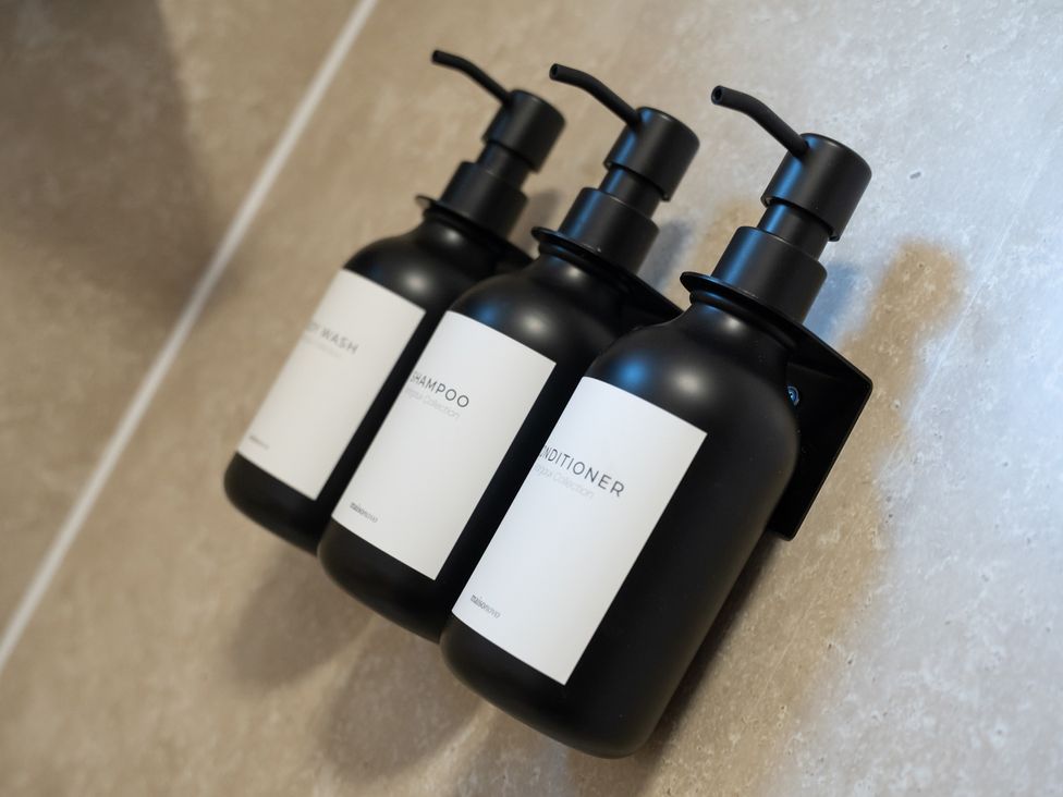 Black bottles of body wash, shampoo, and conditioner in a bathroom at Edison House Stafford