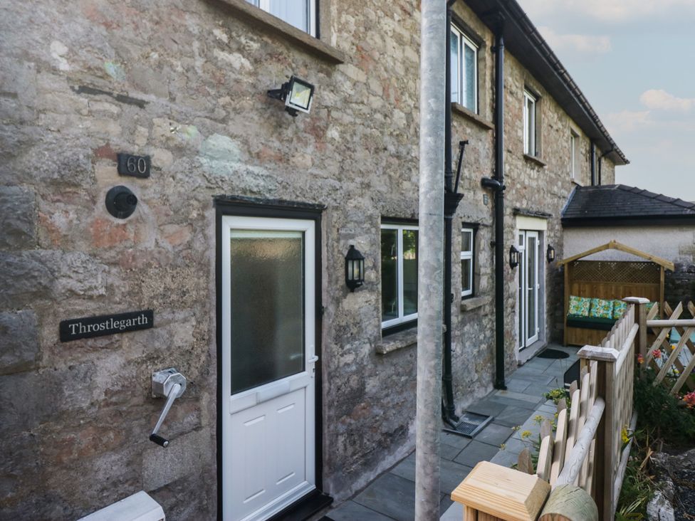 An outdoor view of a stone house with a door and light fixtures at Throstlegarth in Milnthorpe