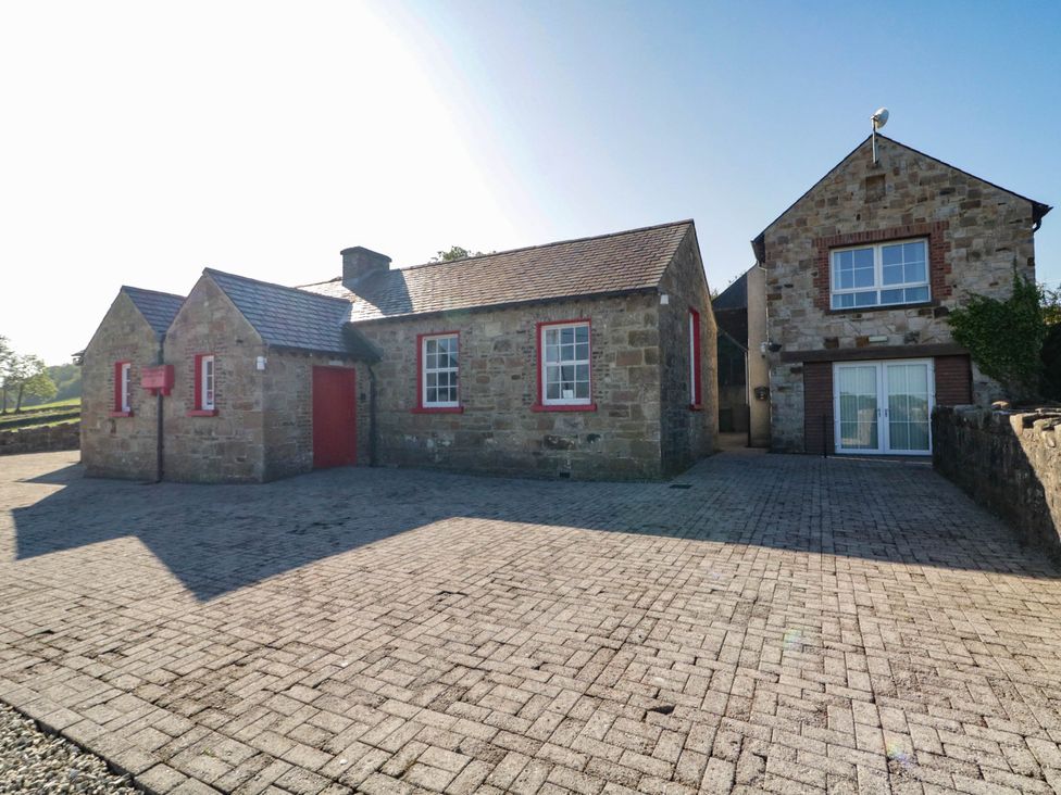 An exterior view of a stone house with red features and a paved driveway at The Mummers Studio Apartment 1 Derrylin, County Fermanagh