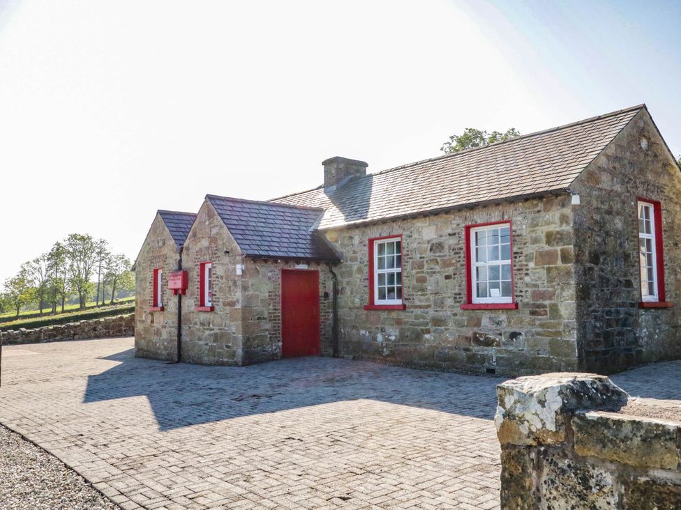 A stone building with red doors and windows in an outdoor area at The Mummers Studio Apartment 1, Derrylin, County Fermanagh