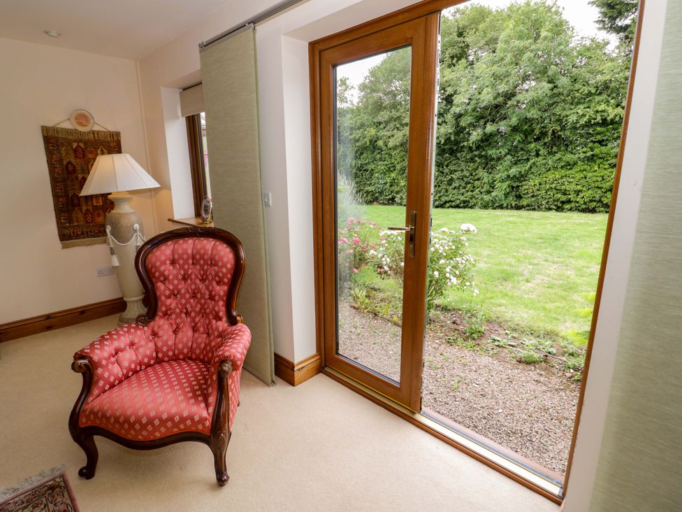 A living room with an armchair and a door leading to a garden at Meadow View Bungalow in Droitwich