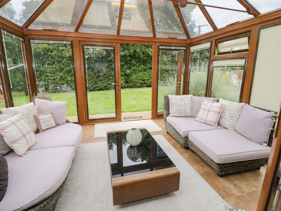 A conservatory with seating area and garden view at Meadow View Bungalow Droitwich