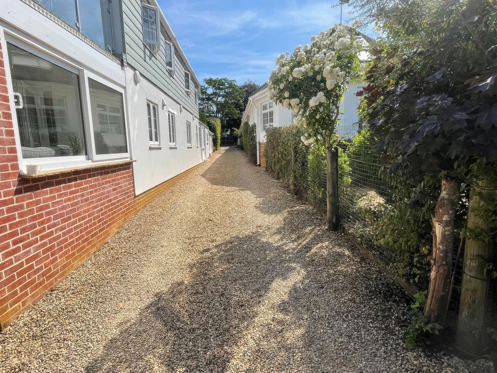 A gravel path between buildings with flowering plants and fences at Bee Hive Hut in Middleton, Norfolk