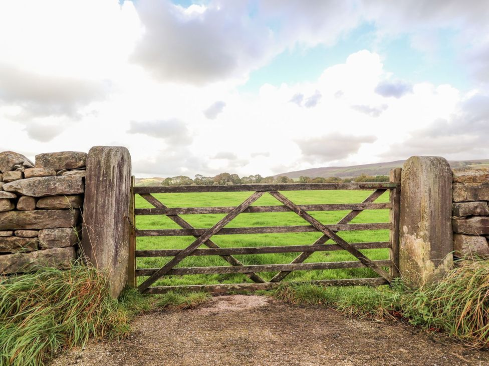 A wooden gate in a stone wall with grass and clouds at Shepherd's Barn in Lancaster