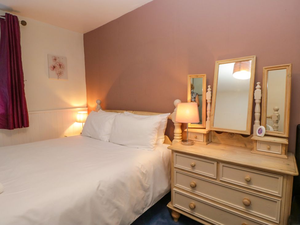 A bedroom with a bed, bedside lamp, and a dressing table at Hillside Cottage in Bowness-On-Windermere