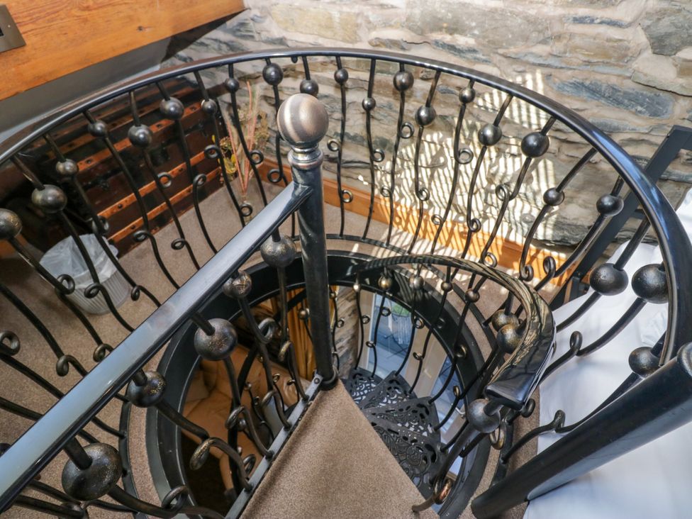 A spiral staircase with a handrail and stone wall at Hillside Cottage Bowness-On-Windermere