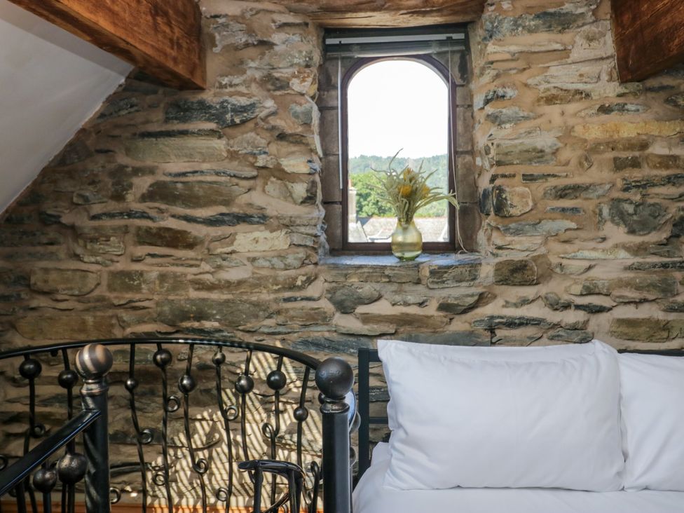 A bedroom with a stone wall and a window at Hillside Cottage in Bowness-On-Windermere