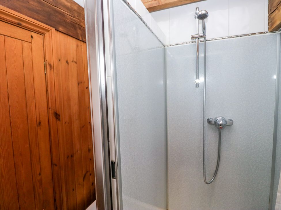A shower with glass enclosure and wooden door at Hillside Cottage in Bowness-On-Windermere