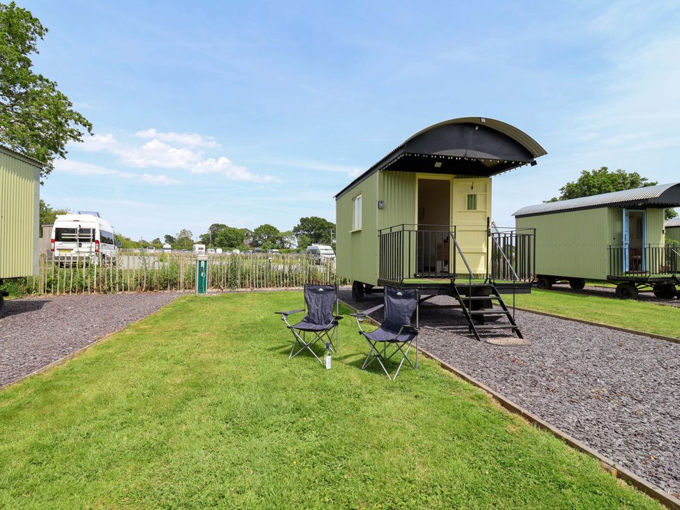 An outdoor area with green cabins and chairs at Bee Happy in Whitchurch