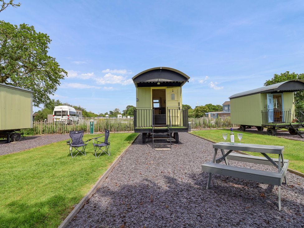 A shepherd's hut with seating and table in the outdoor area at Bee Happy in Whitchurch