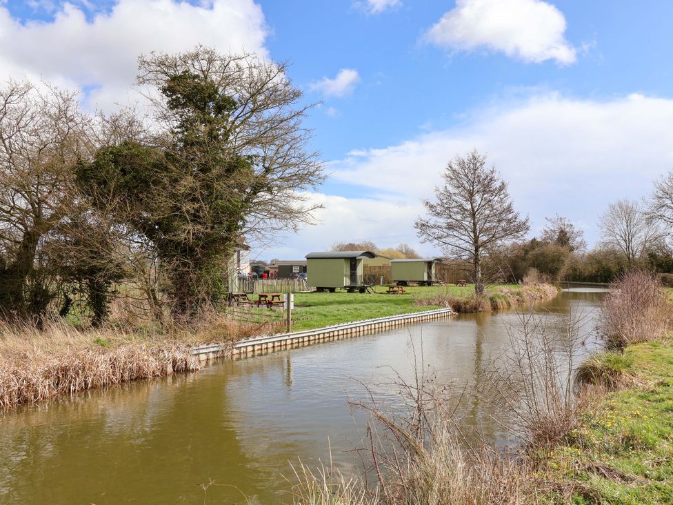 A view of a pond with tree and cabins at Foxes Den in Whitchurch