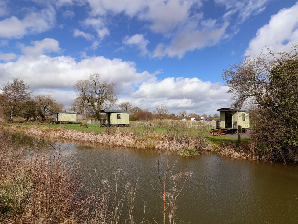 Huts near a pond with trees and grass at Foxes Den in Whitchurch