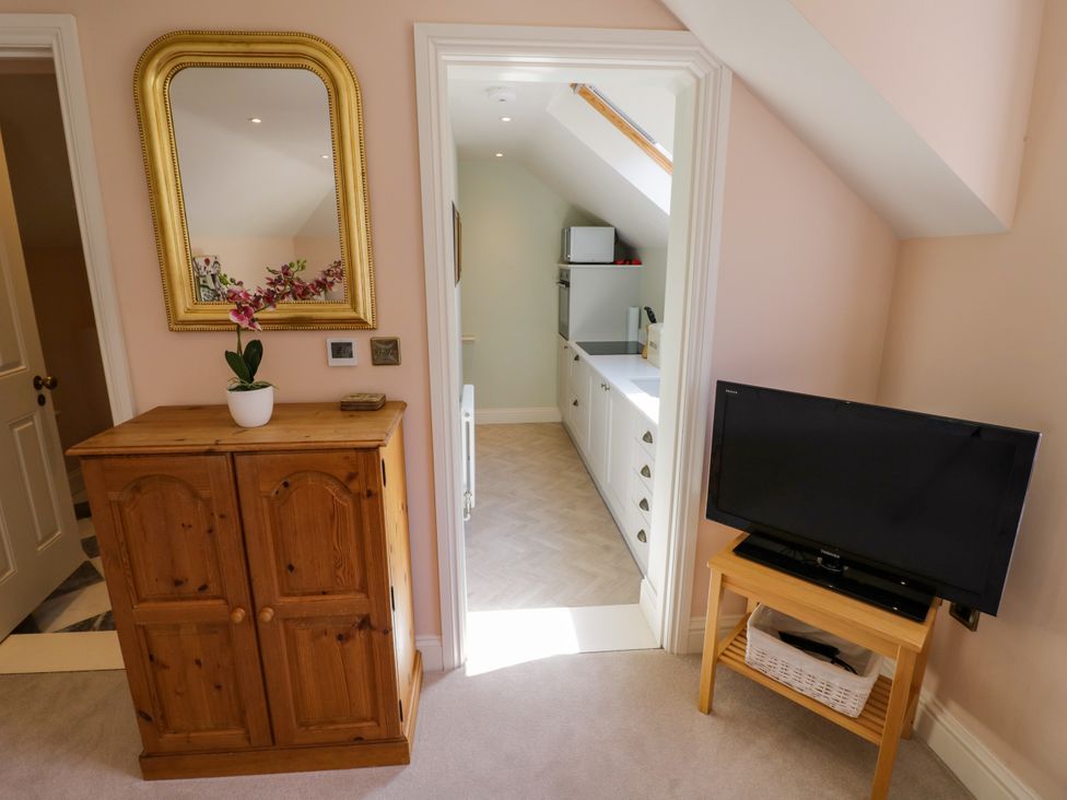 A bedroom with a wooden cabinet and television leading to a kitchen at The Stable Flat
