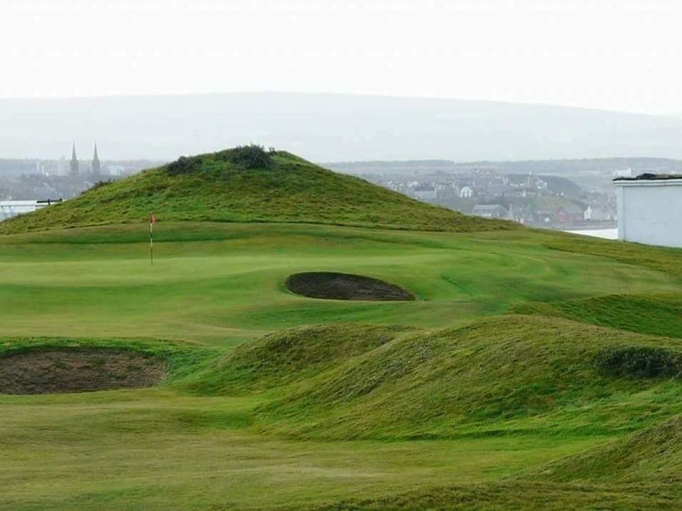 A golf course with a putting green and bunker near a hill
