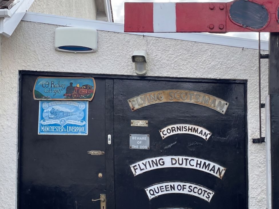 A black entrance door with train-themed signage and a warning sign at 69 Railway Cottages in Manchester