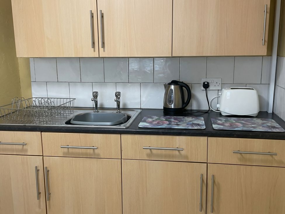 A kitchen with a sink, kettle, toaster, and dish rack at the property