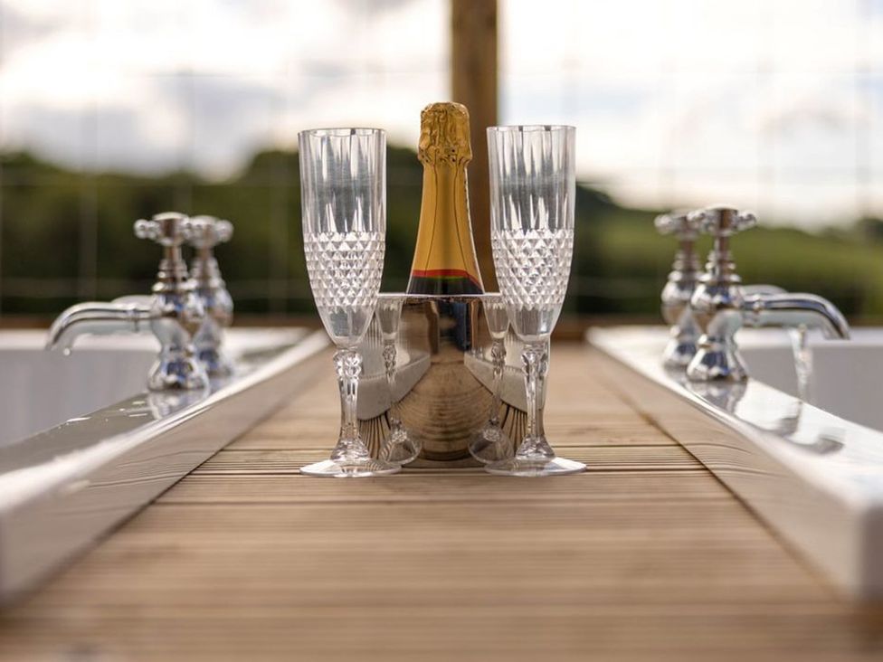 A wooden table with champagne, flutes, and faucets in an outdoor area