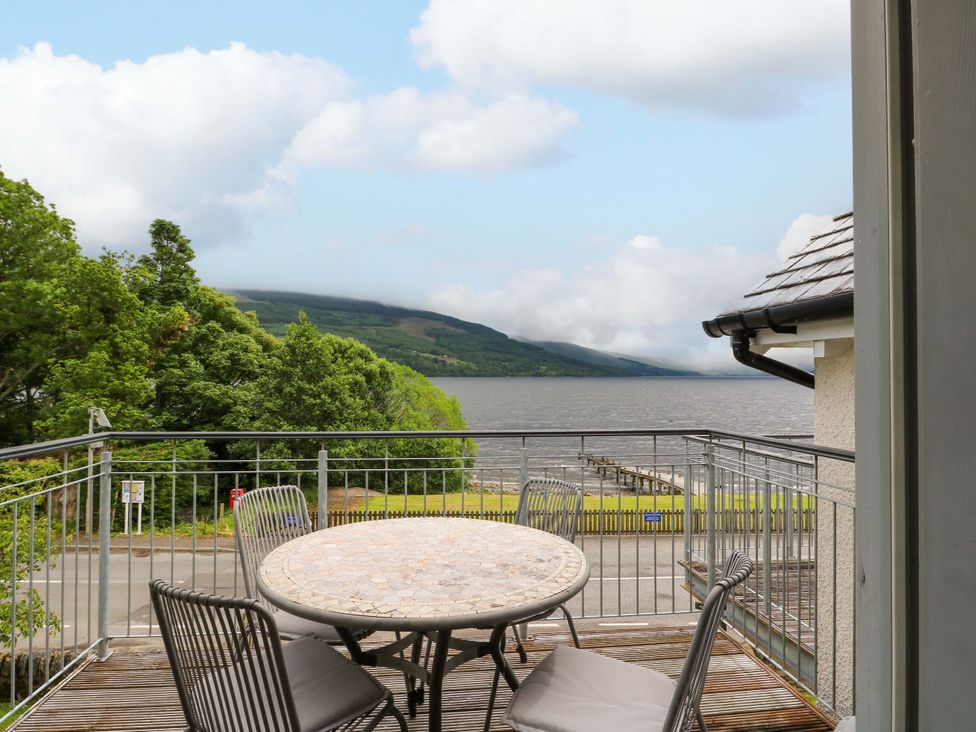 A balcony with a table and chairs overlooking water and mountains at Craigard in Aberfeldy