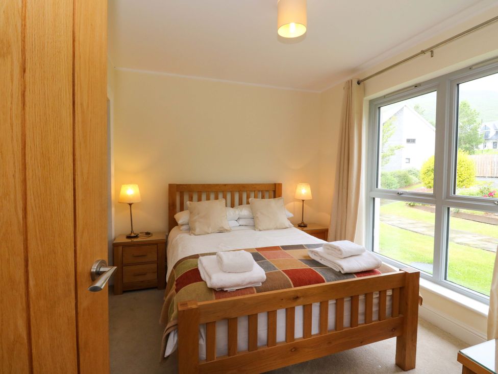 A bedroom with a wooden bed, nightstands, and windows at Craigard in Aberfeldy