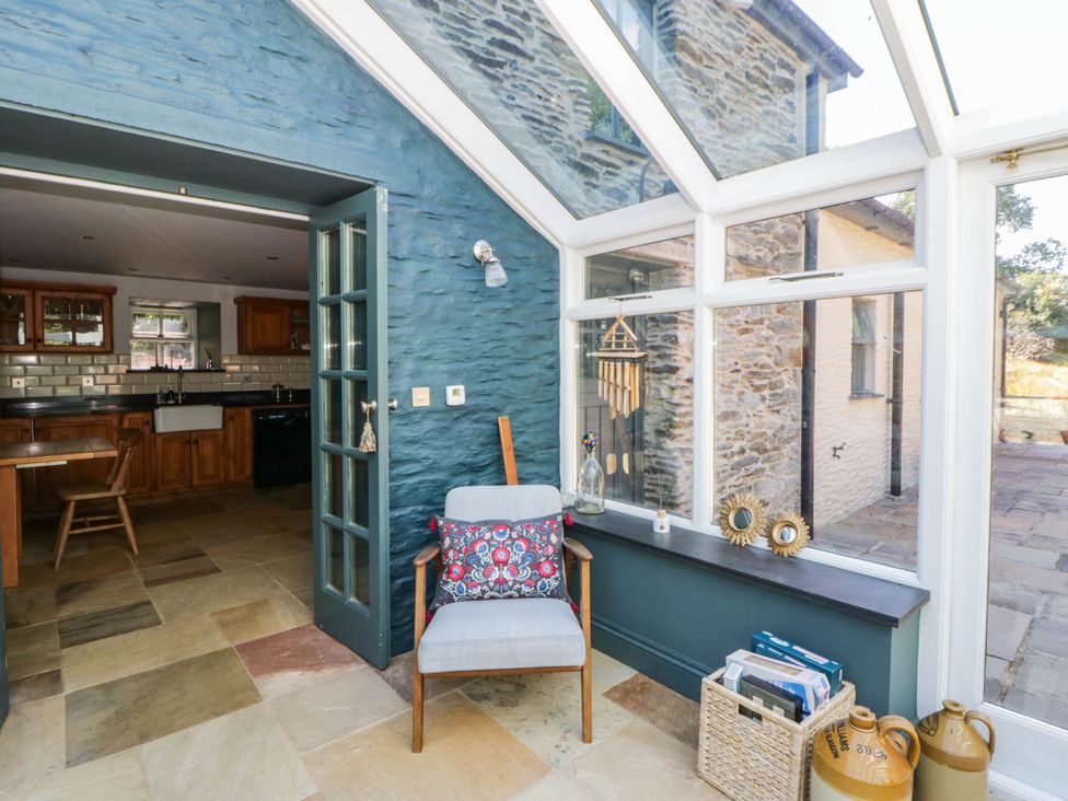 A conservatory with a chair and kitchen view at Yr Hen Felin Boncath