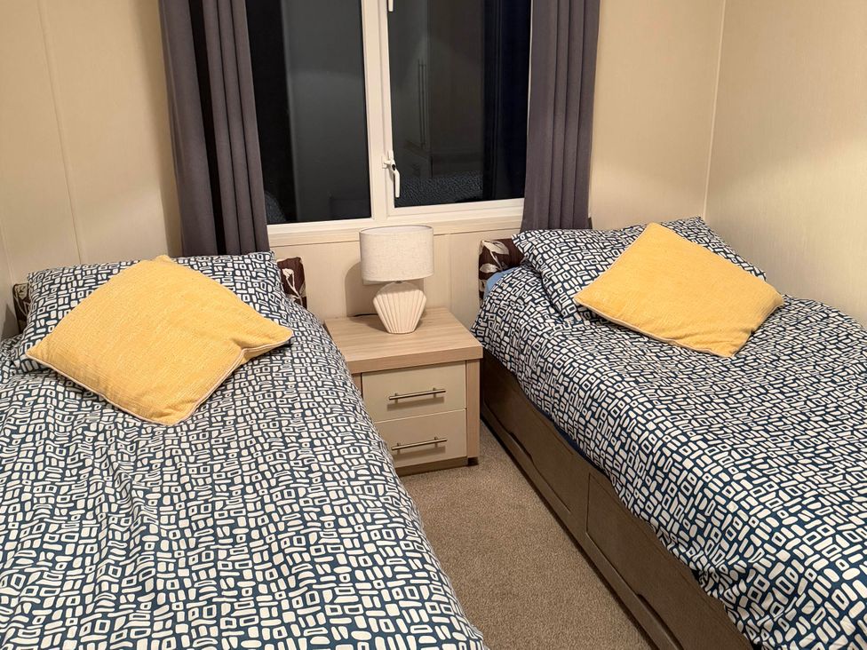 A bedroom with two beds and a bedside table at The Stables in Pwllheli