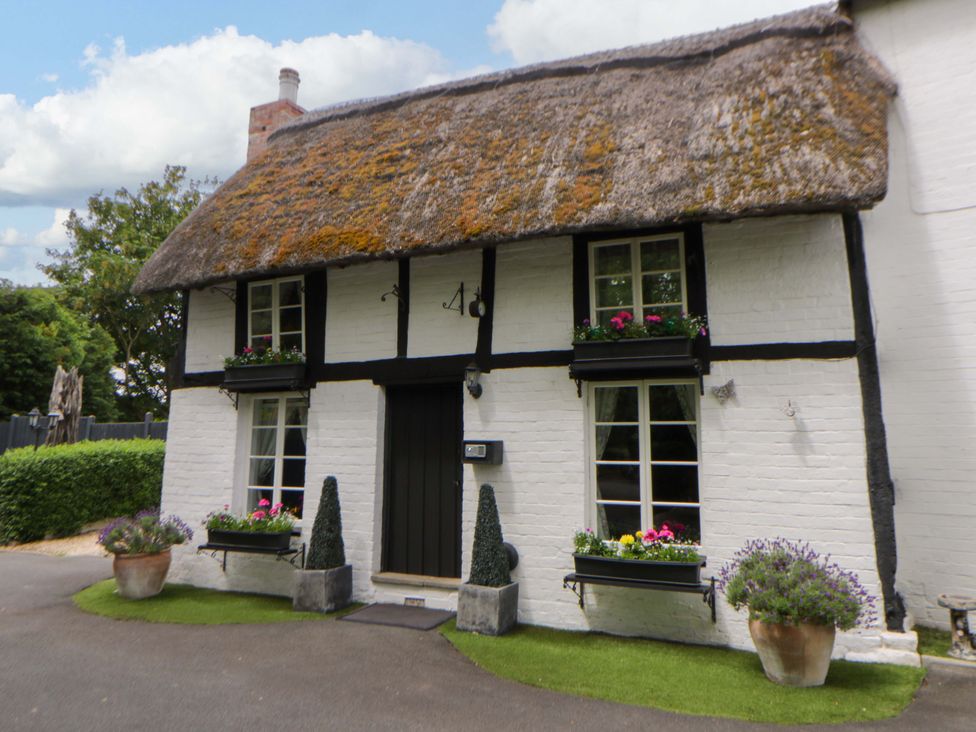 A cottage with a thatched roof and flower planters at Eightlands Hereford