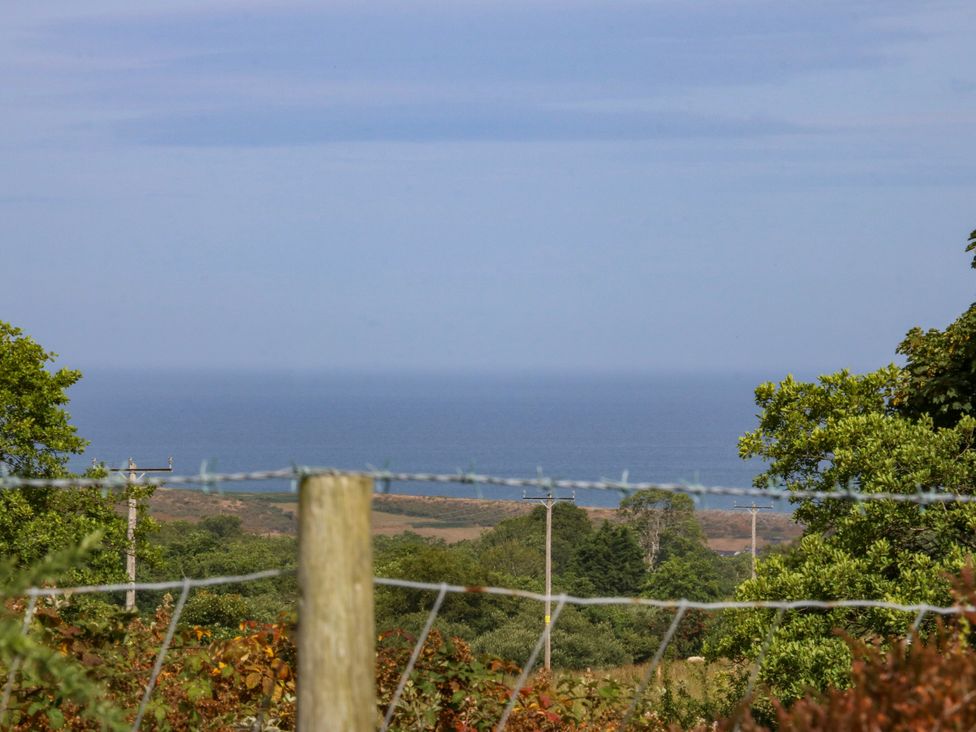 A view of the sea with trees and a fence at Tyr Felin near Trefor