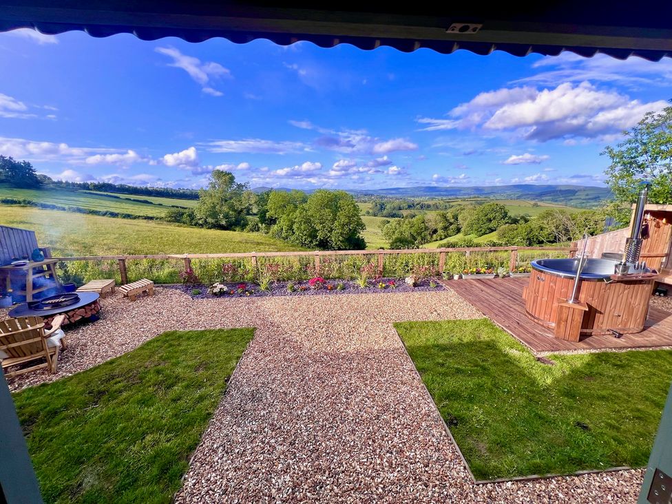 A garden with a wooden hot tub and fire pit at Olive Hut