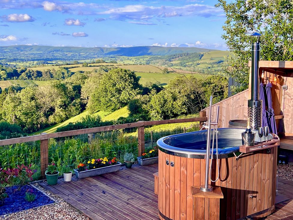 A hot tub on a wooden deck overlooking a landscape at Olive Hut 