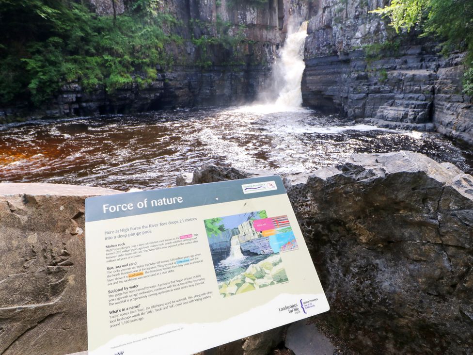 A waterfall with rocks and a sign at High Force in Middleton-In-Teesdale