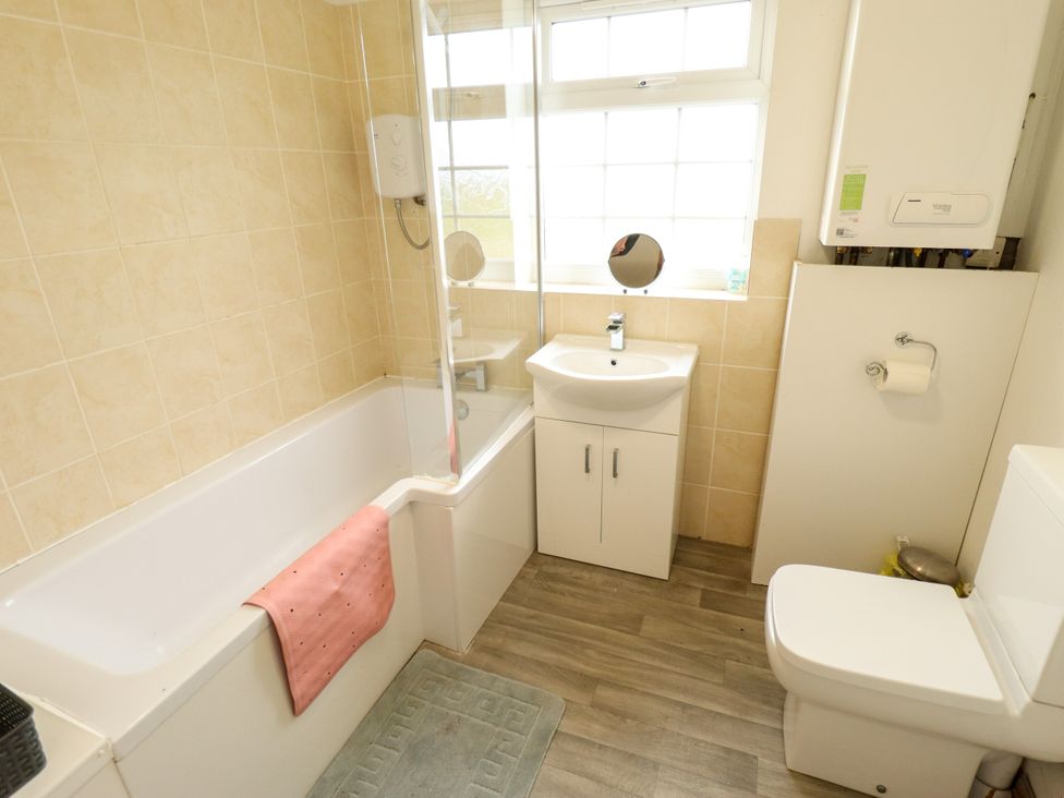 A bathroom with a bath, toilet, sink and mirror at Holiday Cottage 3 in Skegness