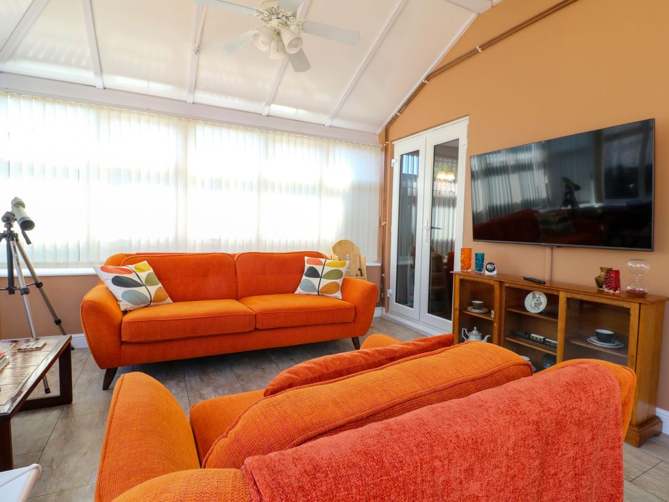 A conservatory with orange sofas and a television at Pinecote Cottage Nottingham