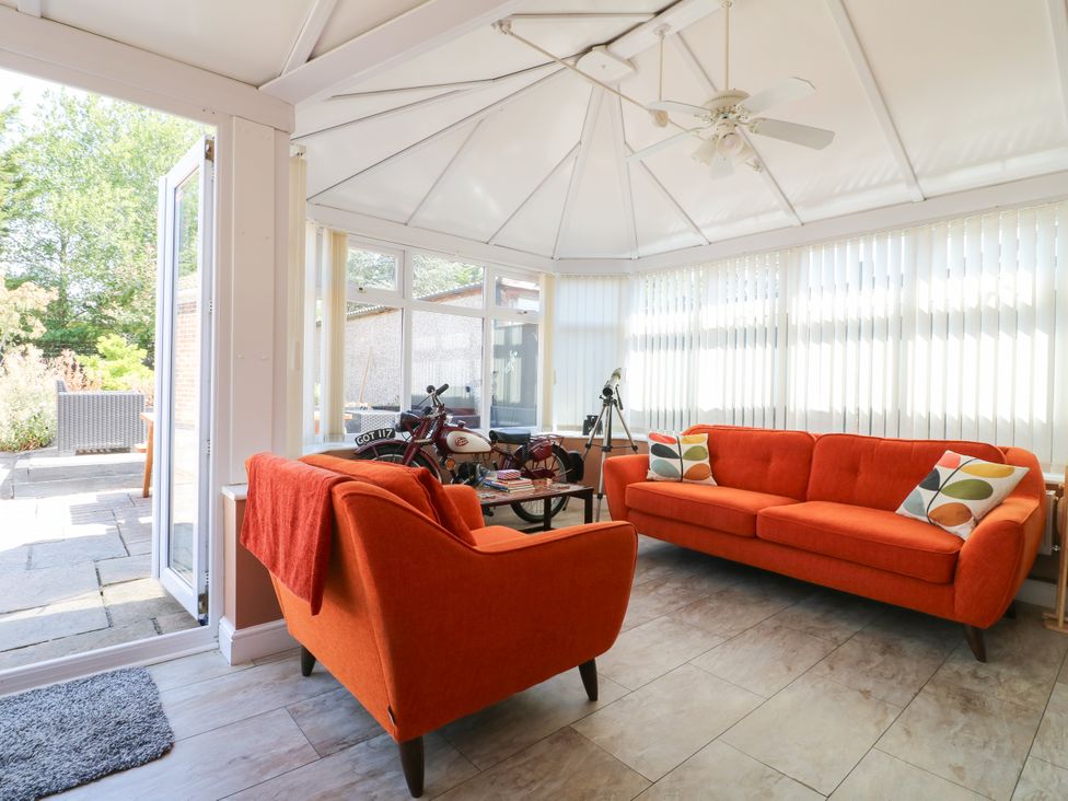 A conservatory with orange sofas and a coffee table at Pinecote Cottage in Nottingham