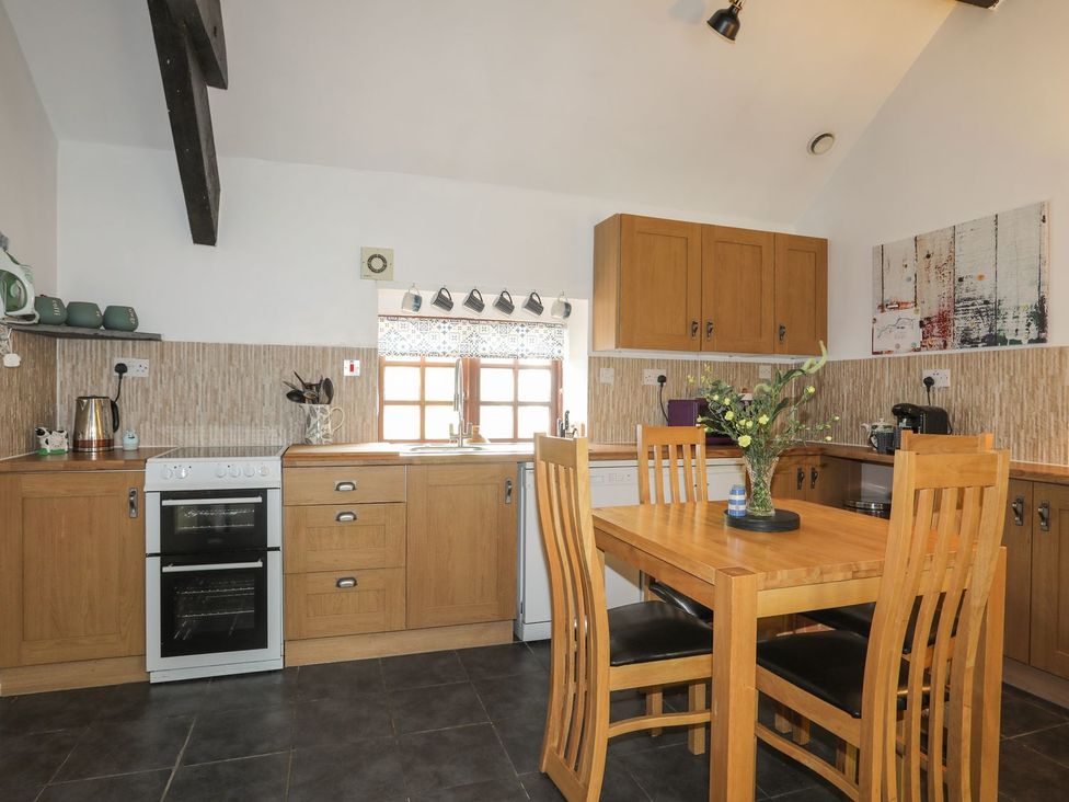A kitchen with wooden cabinets and a dining table at Riverside Cottage in Caernarfon