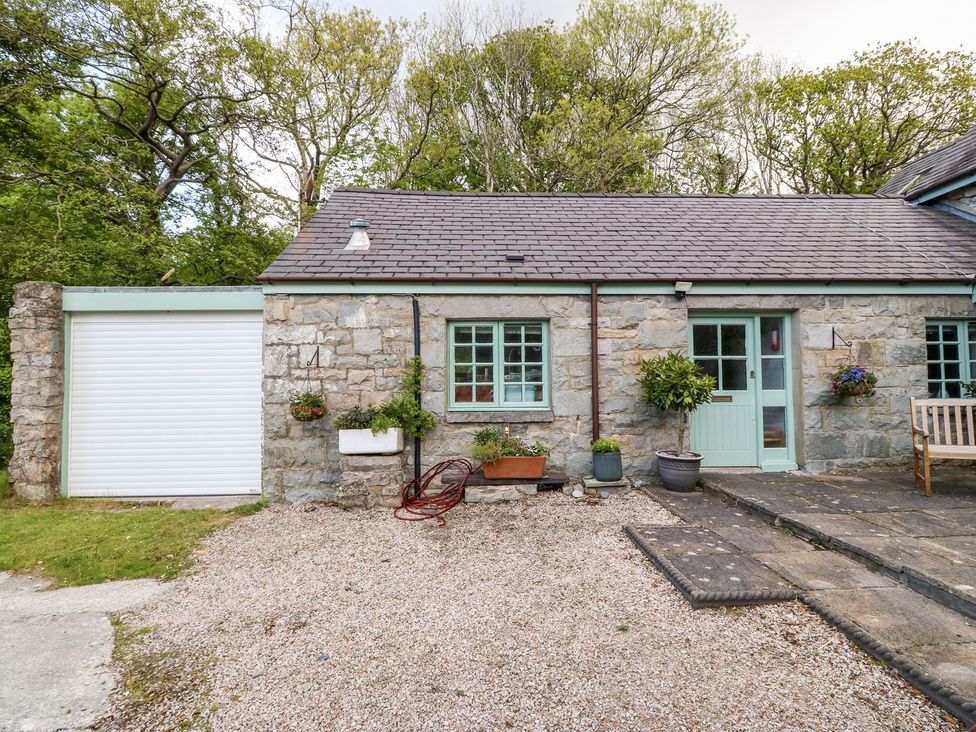 A cottage exterior with stone wall, garage door and plants at Riverside Cottage in Caernarfon