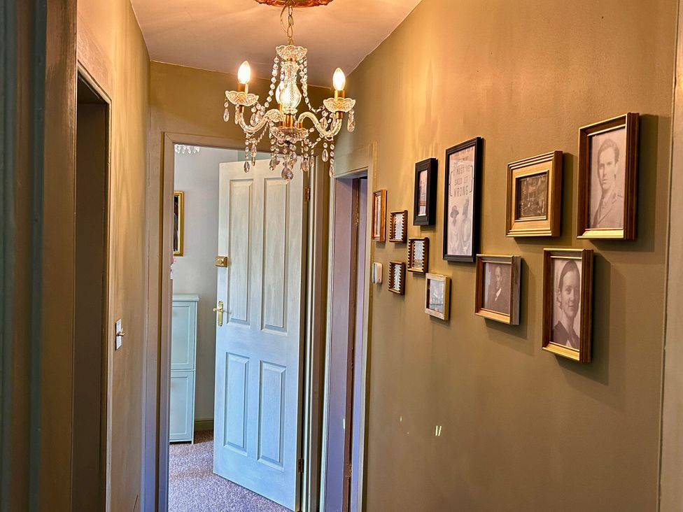 A hallway with a chandelier and framed photographs at Downton II in Alnwick