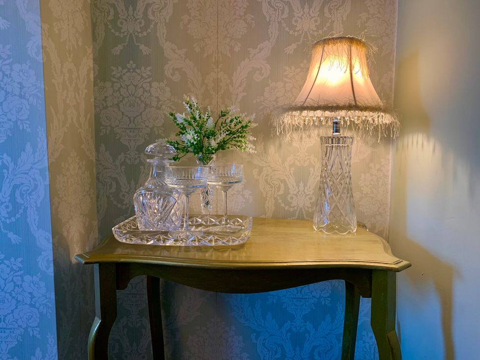 A table with a lamp, flower arrangement, decanter, and glasses at Downton II in Alnwick